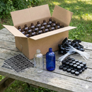 Box of glass bottles, labels, and caps on a wooden table outdoors.